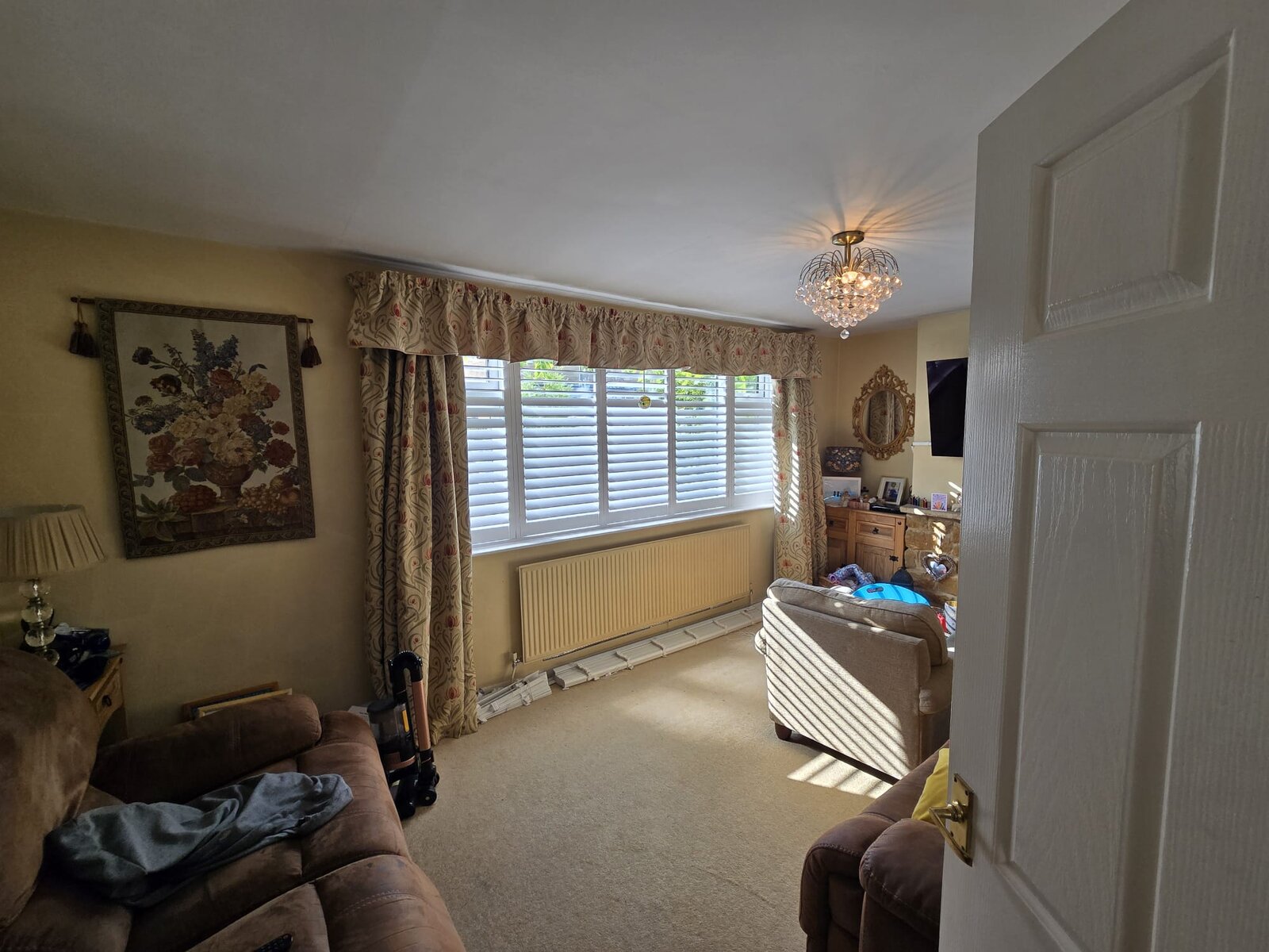 Chacombe living room with white full-height hardwood shutters across a wide window, sofa and stone fireplace