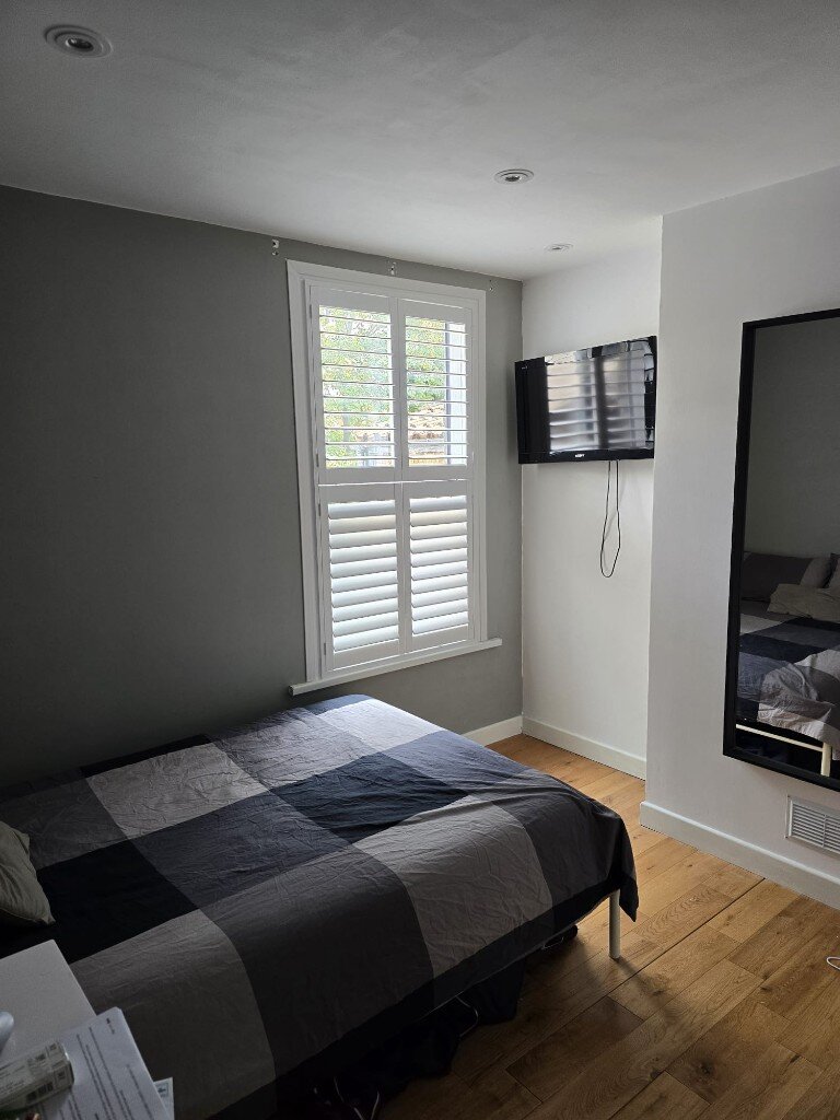 Hardwood tier-on-tier shutters in a Croydon bedroom with the top tier open and the bottom closed