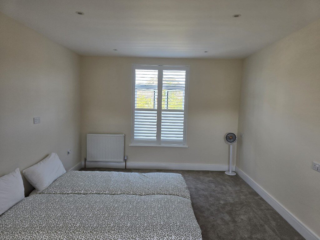 Full-height white shutters on a Harrow bedroom window with the top louvres open and the bottom closed