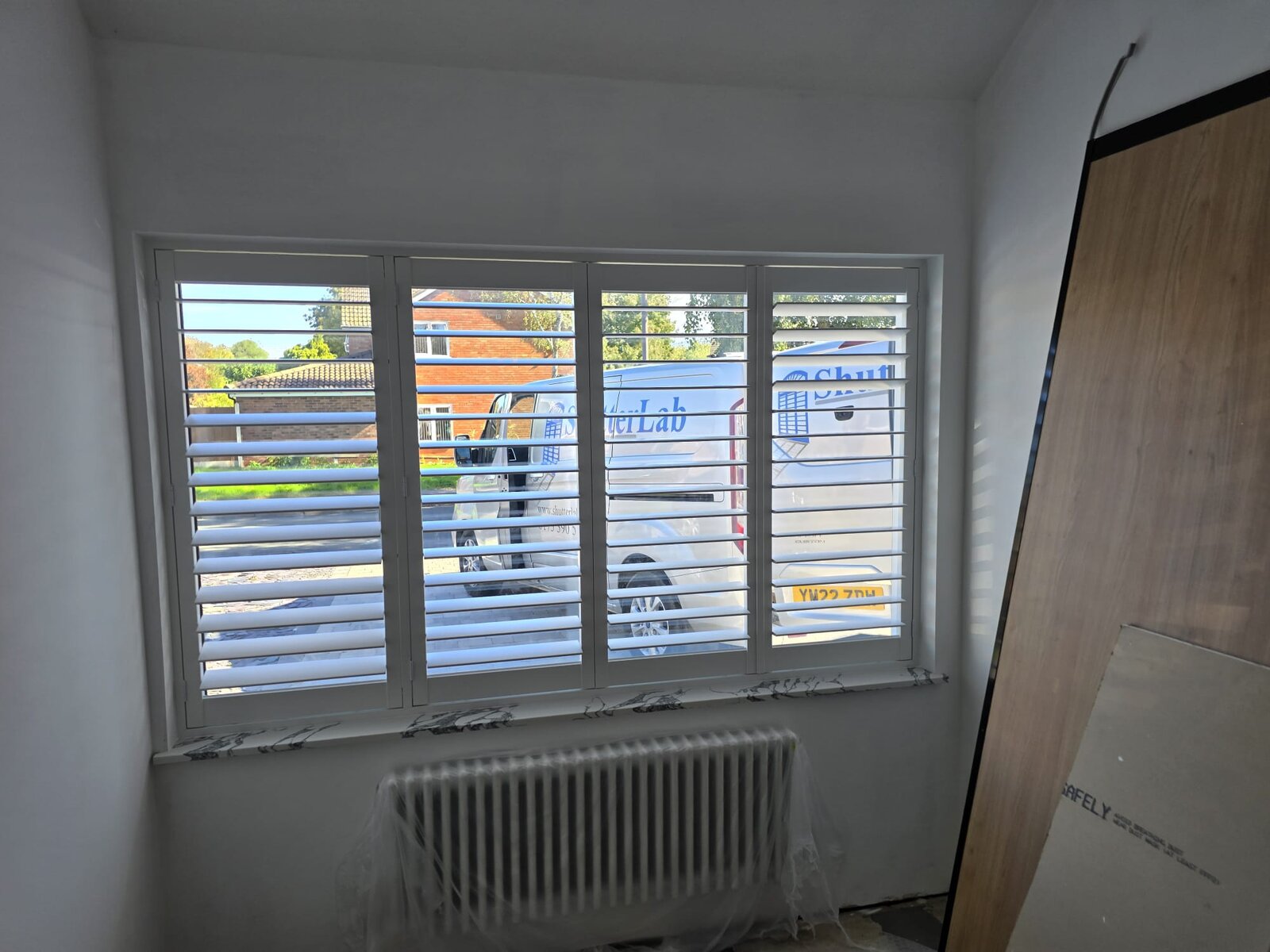 Four-panel white hardwood shutters with 89mm louvres open on a Leamington Spa living-room window