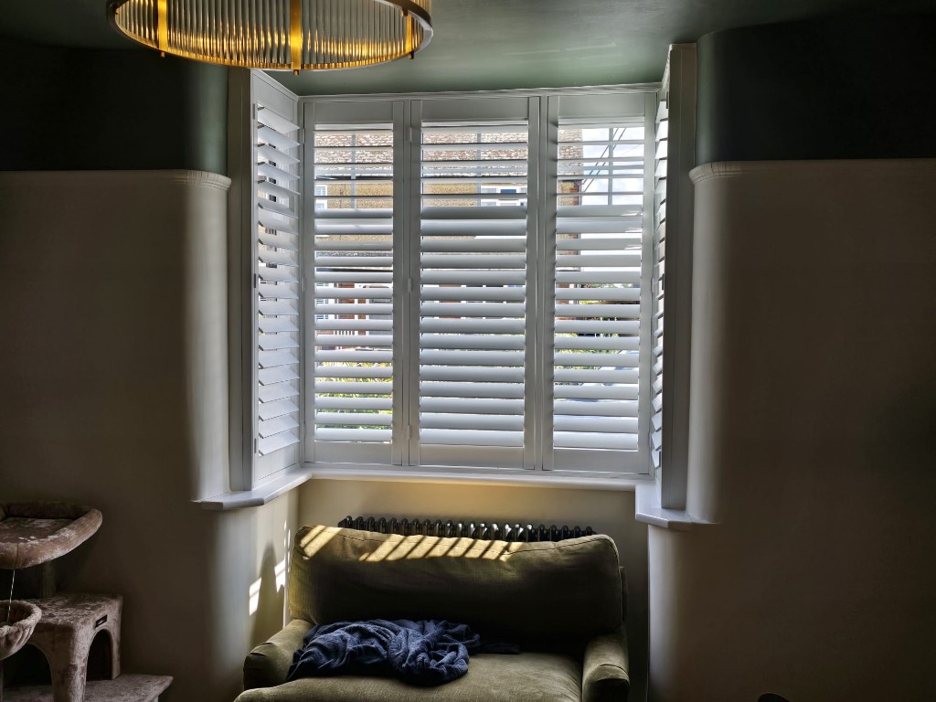 Close view of Snow White full-height hardwood bay shutters with louvres open in Northampton