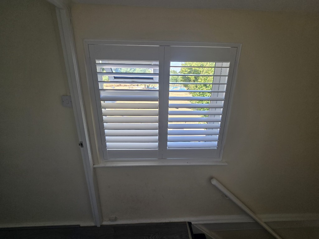 White full-height polymer shutters on a staircase landing window with louvres open