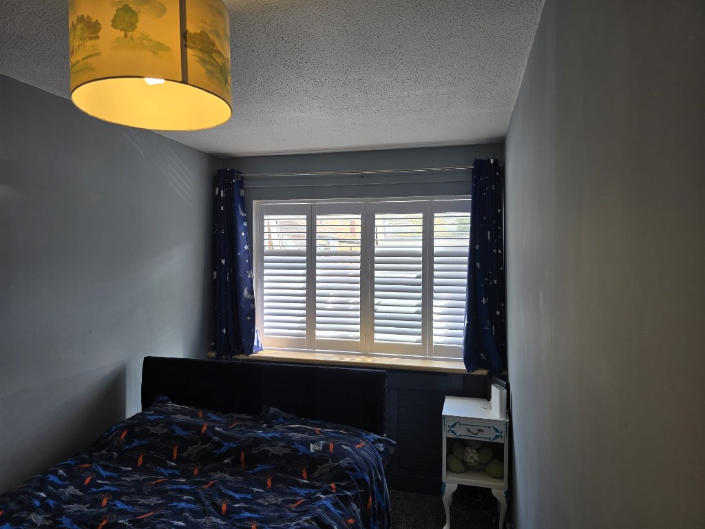 Snow White full-height hardwood shutters on a bedroom window with navy star-pattern curtains