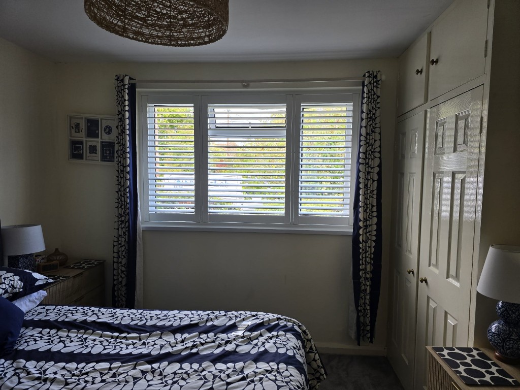 Snow White full-height polymer shutters on a Wallingford bedroom window with navy floral curtains
