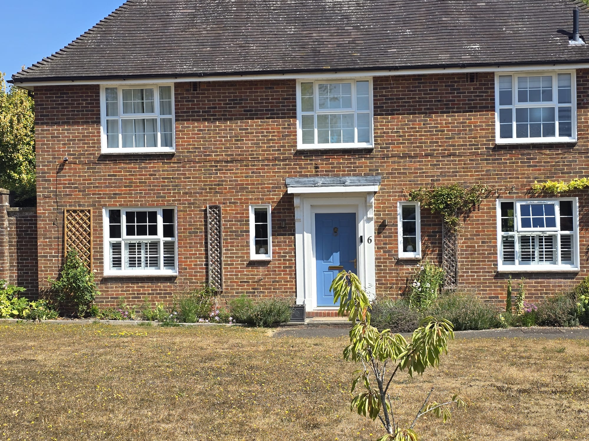 White café-style hardwood shutters on the ground-floor windows of a red-brick Winchester home